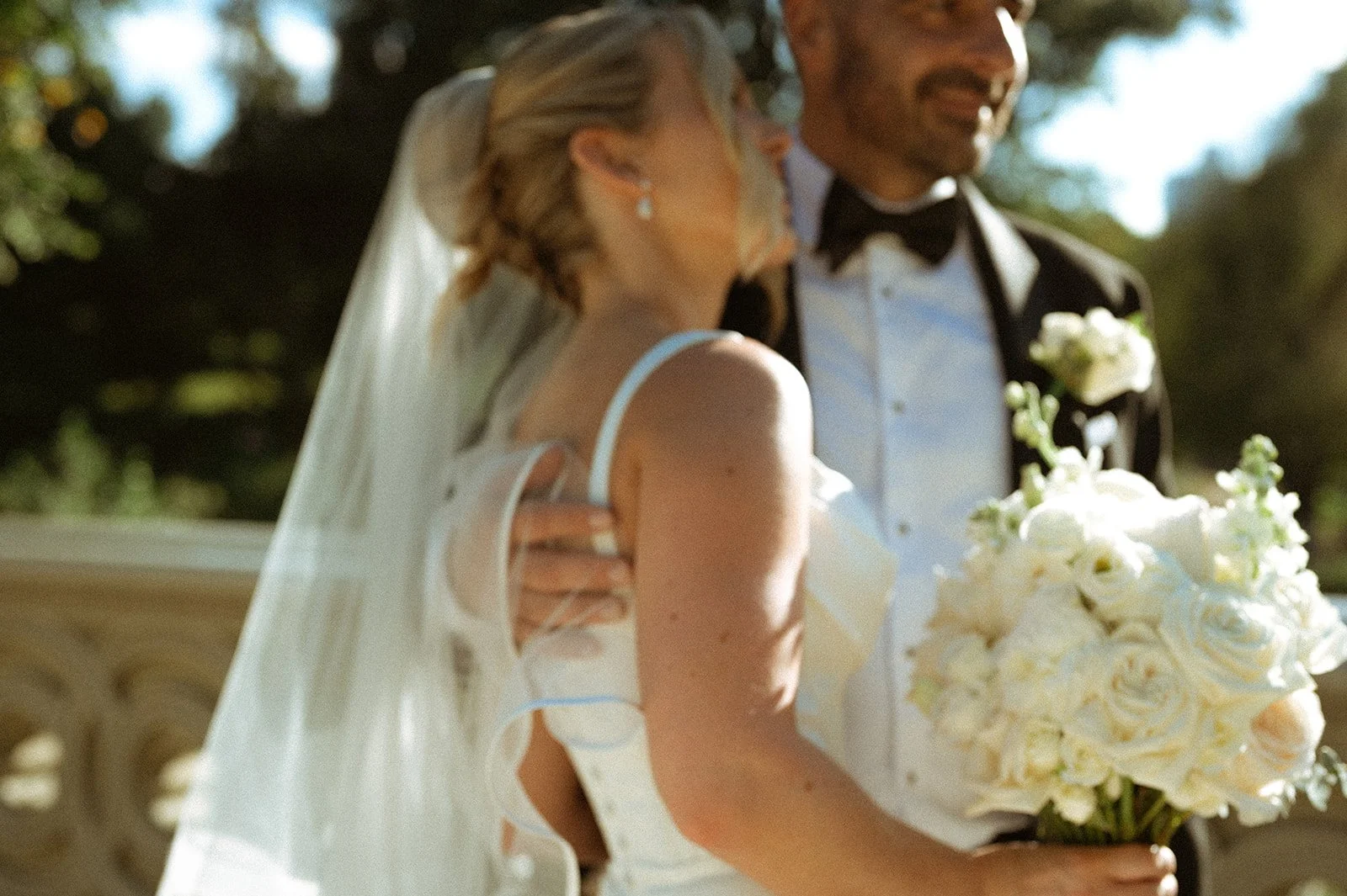 Bride and groom embracing on Bow Bridge in Central Park, holding a bouquet of white flowers.