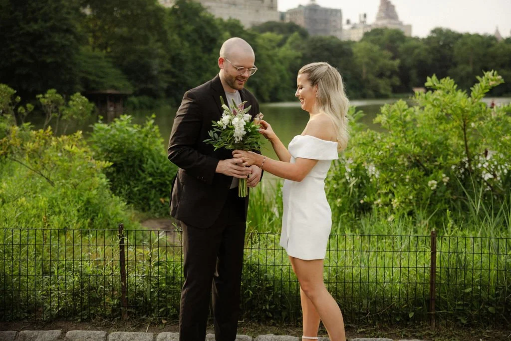 Bride and groom outdoors in Central Park with greenery and water behind them.