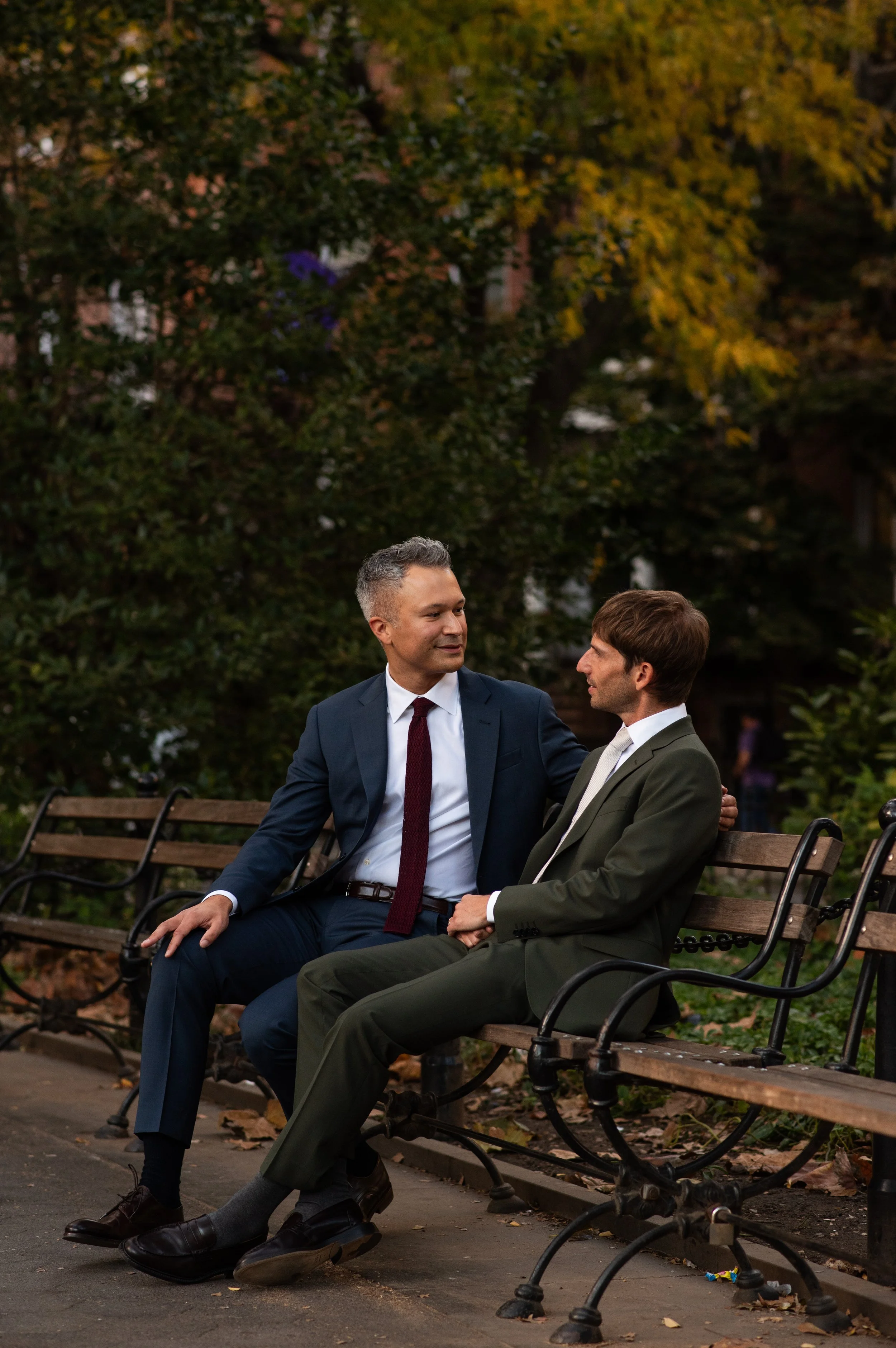 Two men sitting on a bench in Washington Square Park surrounded by fall foliage before their Cakewalk elopement ceremony.