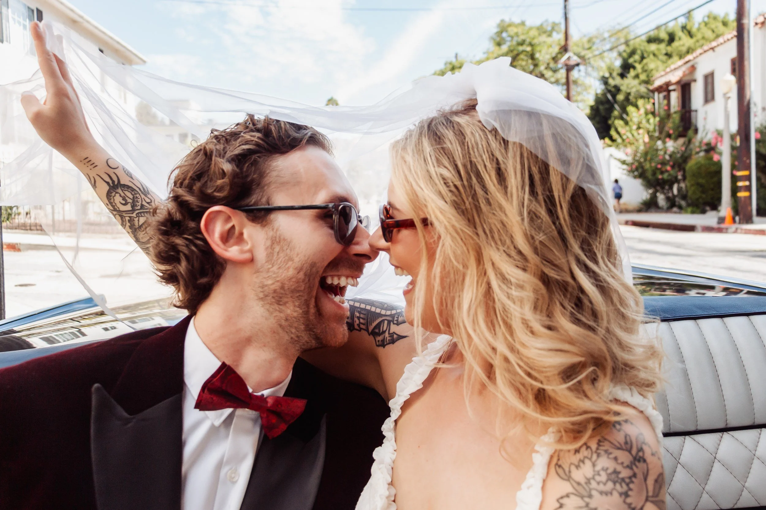 Emma and Adam laughing under her veil in a vintage Lincoln during their Los Angeles elopement.