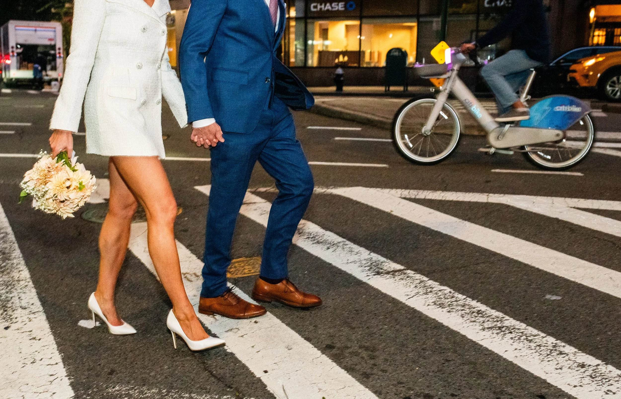 Bride and groom crossing the street in the West Village, a biker passing behind them, after their Cakewalk elopement ceremony.