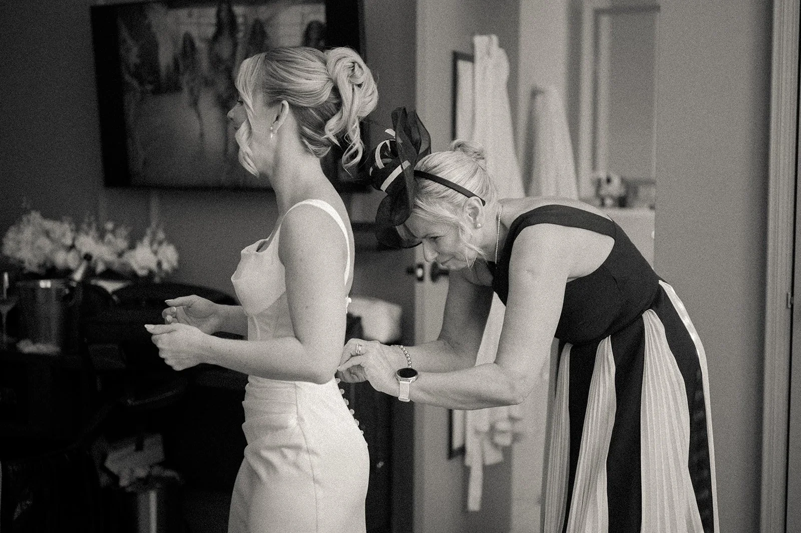 Bride getting ready for her Cakewalk, a family member helping her button up her dress in the hotel.
