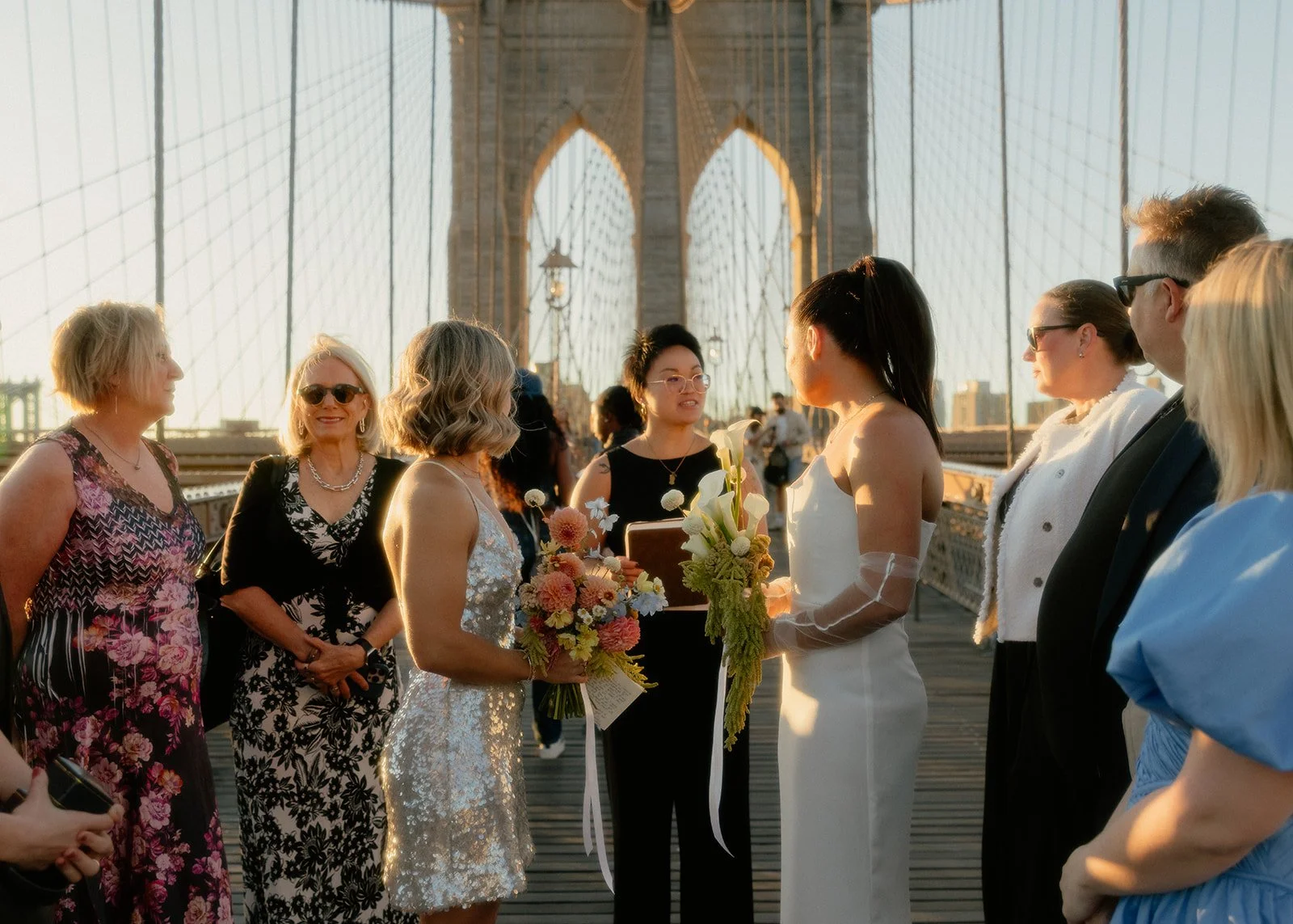 LGBT brides being married by their Cakewalk officiant on the Brooklyn Bridge at sunrise surrounded by their group of guests.