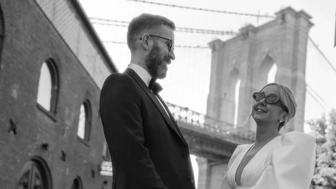 Bride and groom wearing sunglasses standing in front of the Brooklyn Bridge at the Brooklyn Heights Promenade