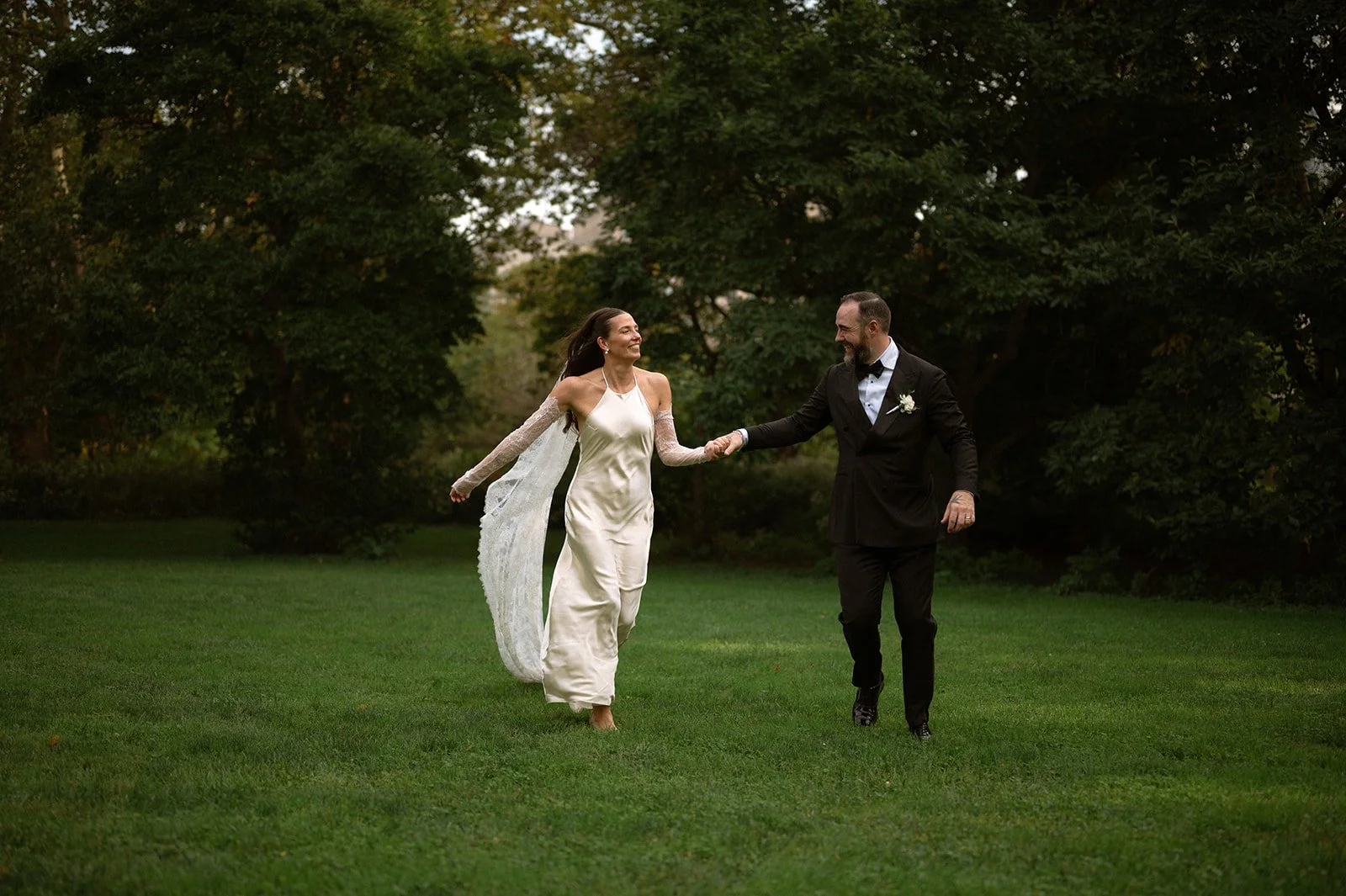 Bride and groom running across the grass in Central Park after their Cakewalk micro wedding.