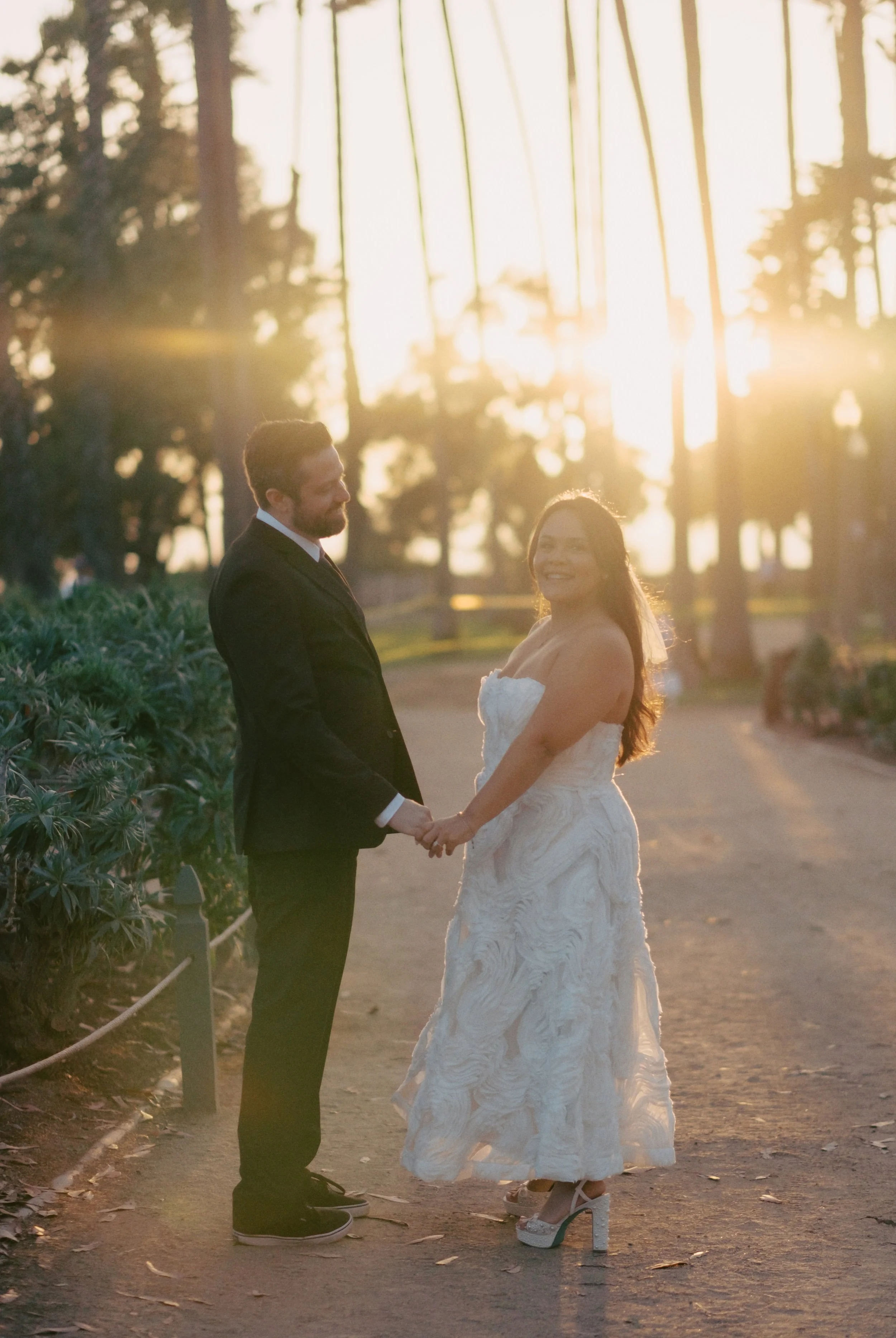 Bride and groom standing in the dirt path in Palisades Park in Santa Monica among the palm trees and sunset after their Cakewalk elopement ceremony.