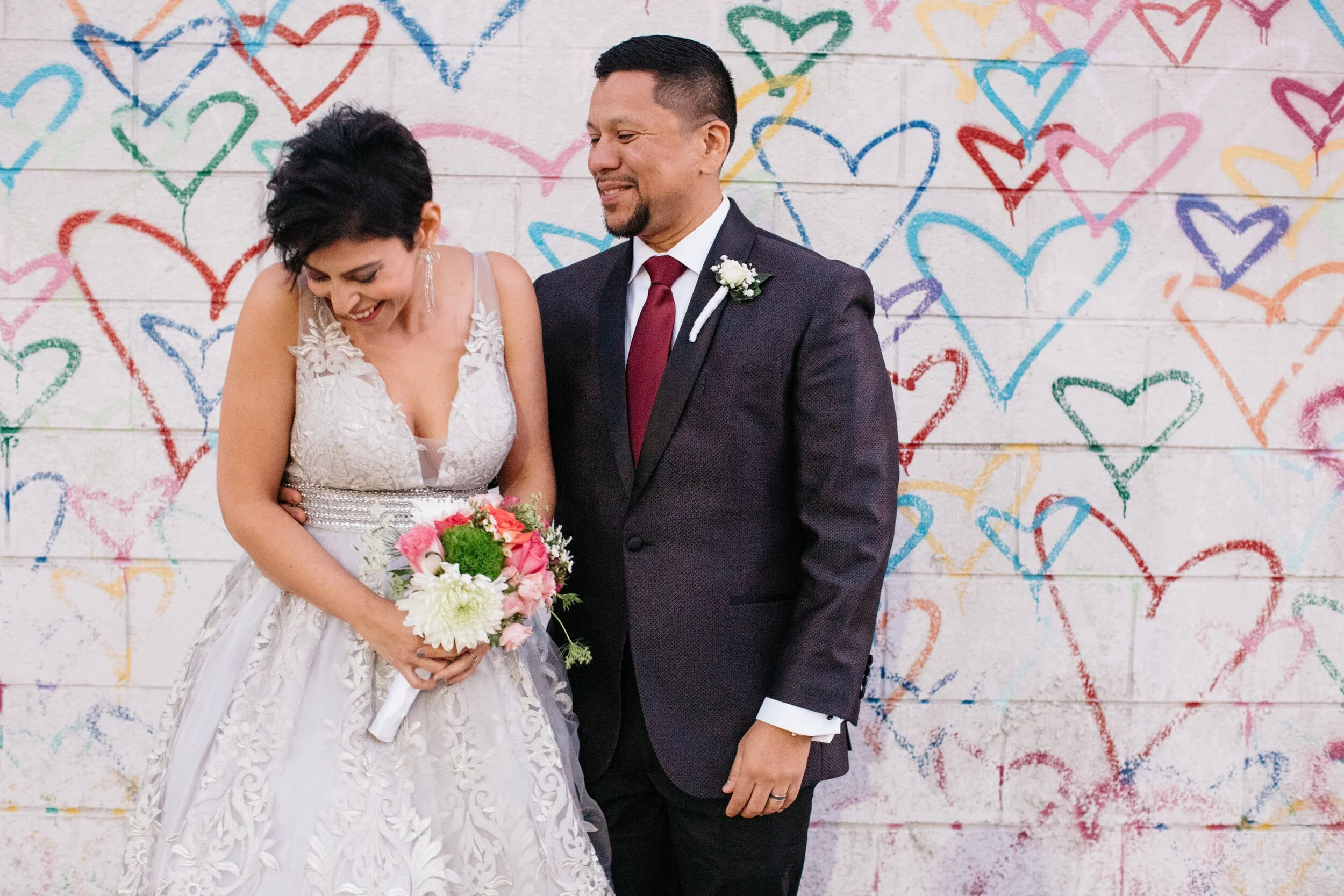 Couple laughing in front of colorful DC heart mural, bride holding vibrant bouquet, elopement.