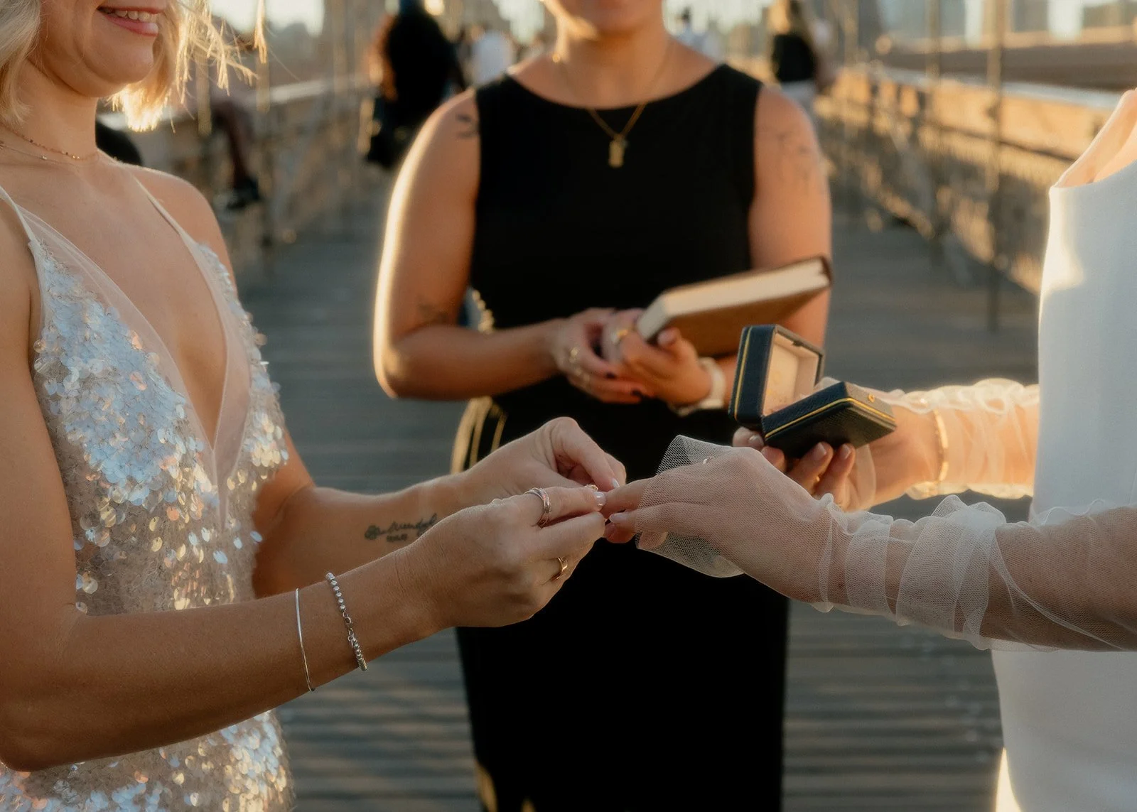 LGBT brides exchanging rings at their Cakewalk elopement on the Brooklyn Bridge at sunrise with their officiant behind them.