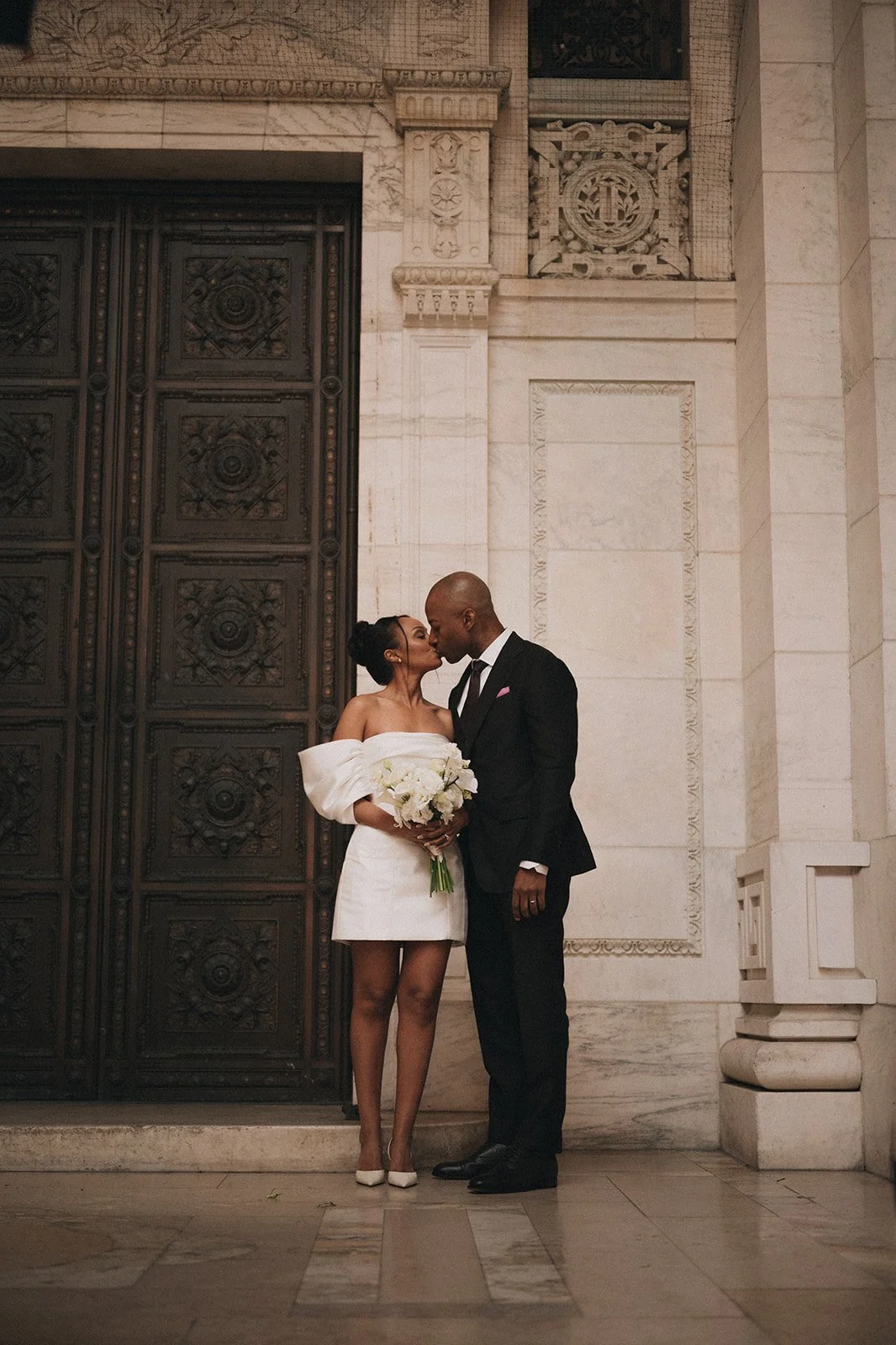 Bride and groom kissing in front of a large door at the New York Public Library after their Cakewalk wedding ceremony.