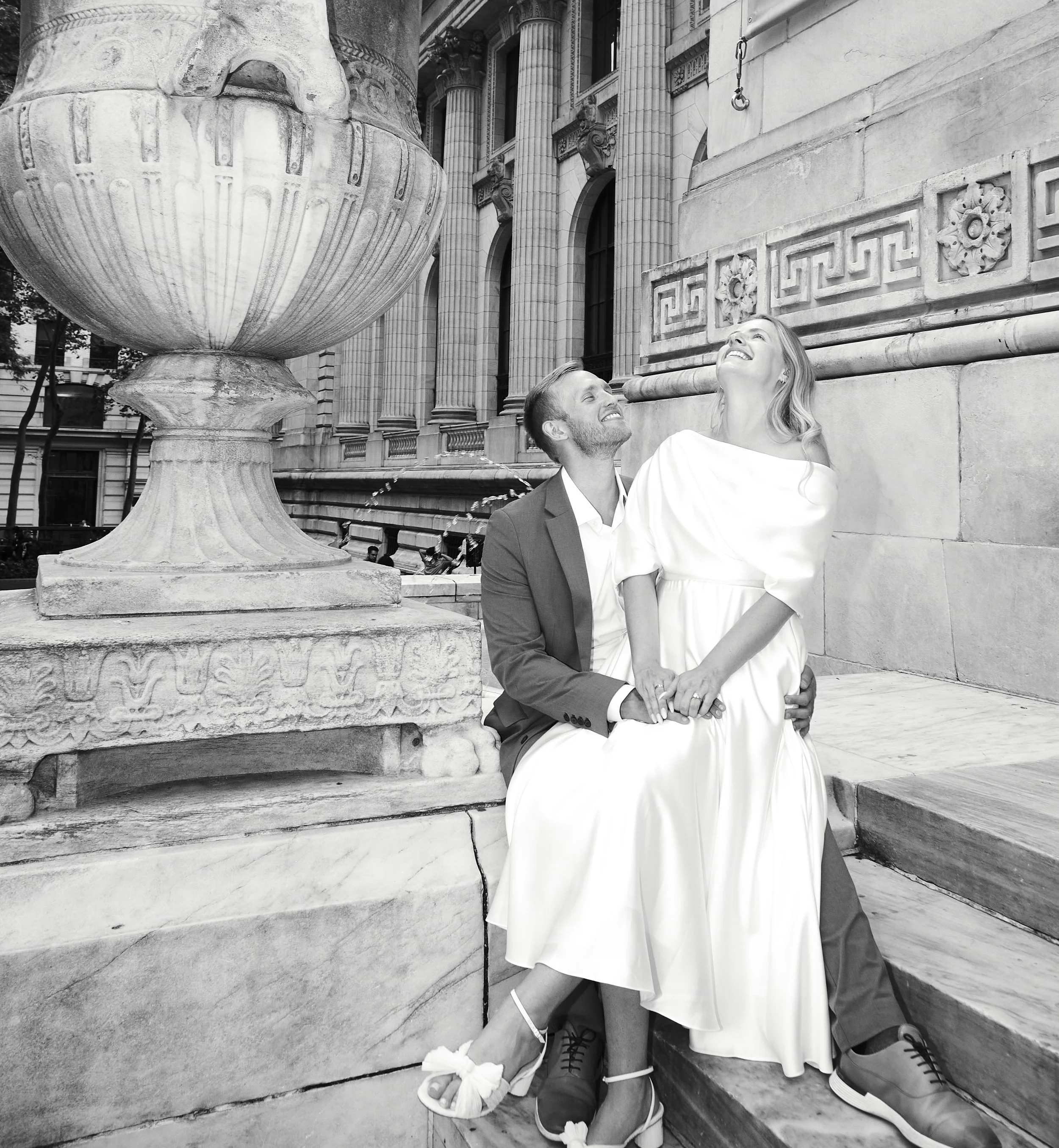 Bride and groom sitting near sculptures and laughing in Rockefeller Center after their Cakewalk elopement.