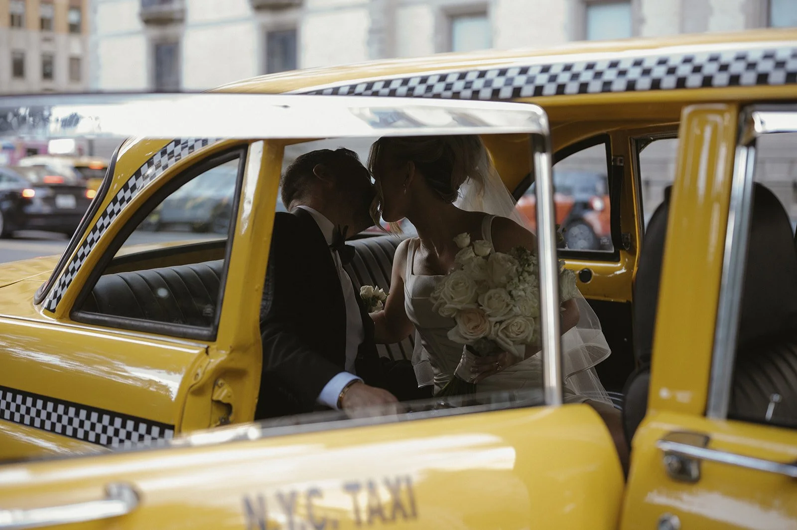 Bride and groom kissing inside a vintage, yellow checkered NYC taxi on the streets of Manhattan.