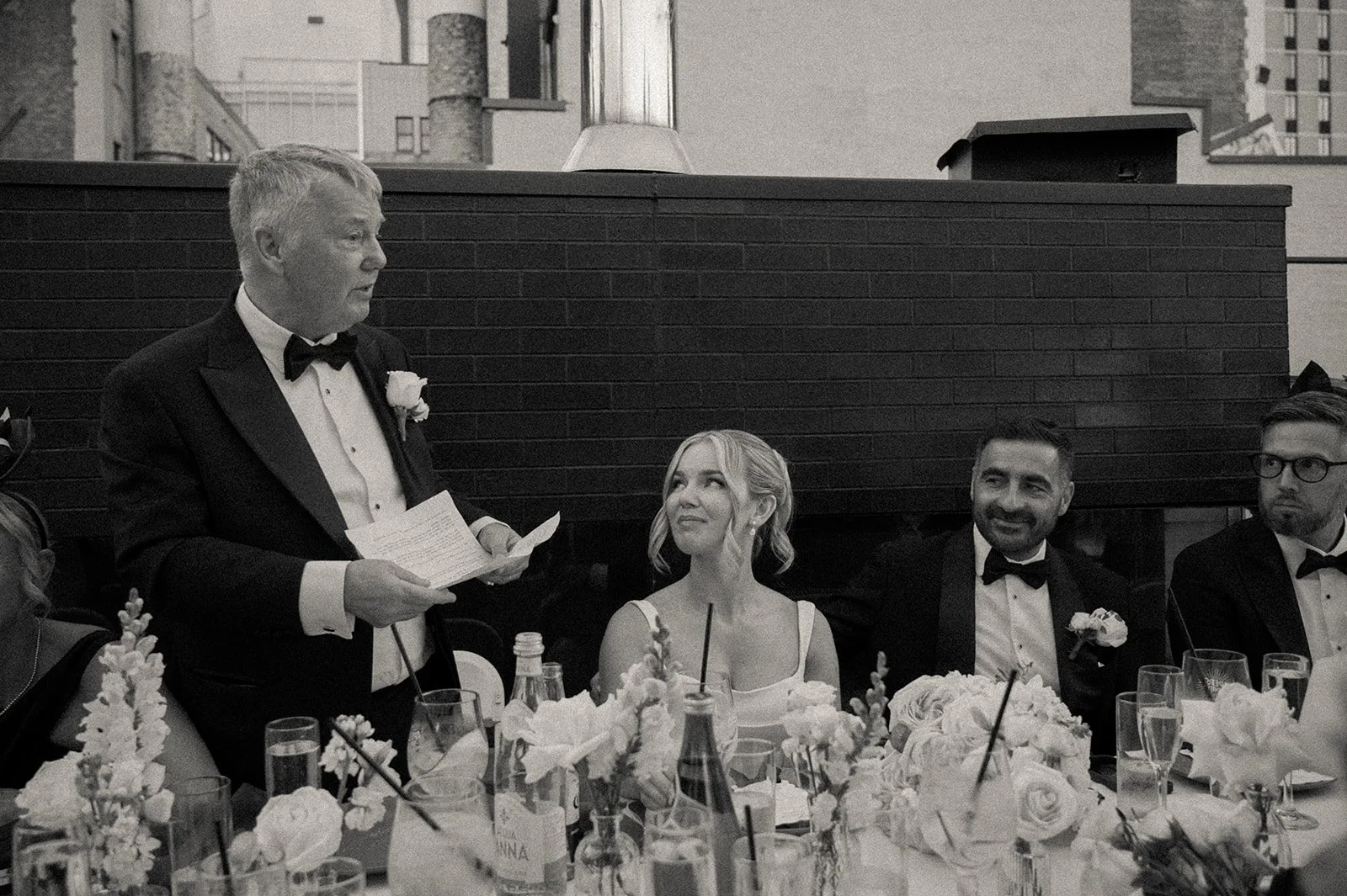 Bride and groom seated at dinner while the father of the bride reads a speech at Rosehill in Manhattan.
