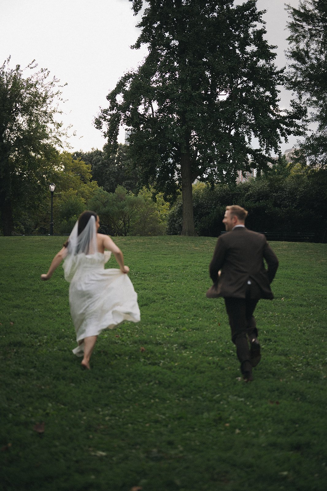 Bride and groom running on lush grass in Central Park.