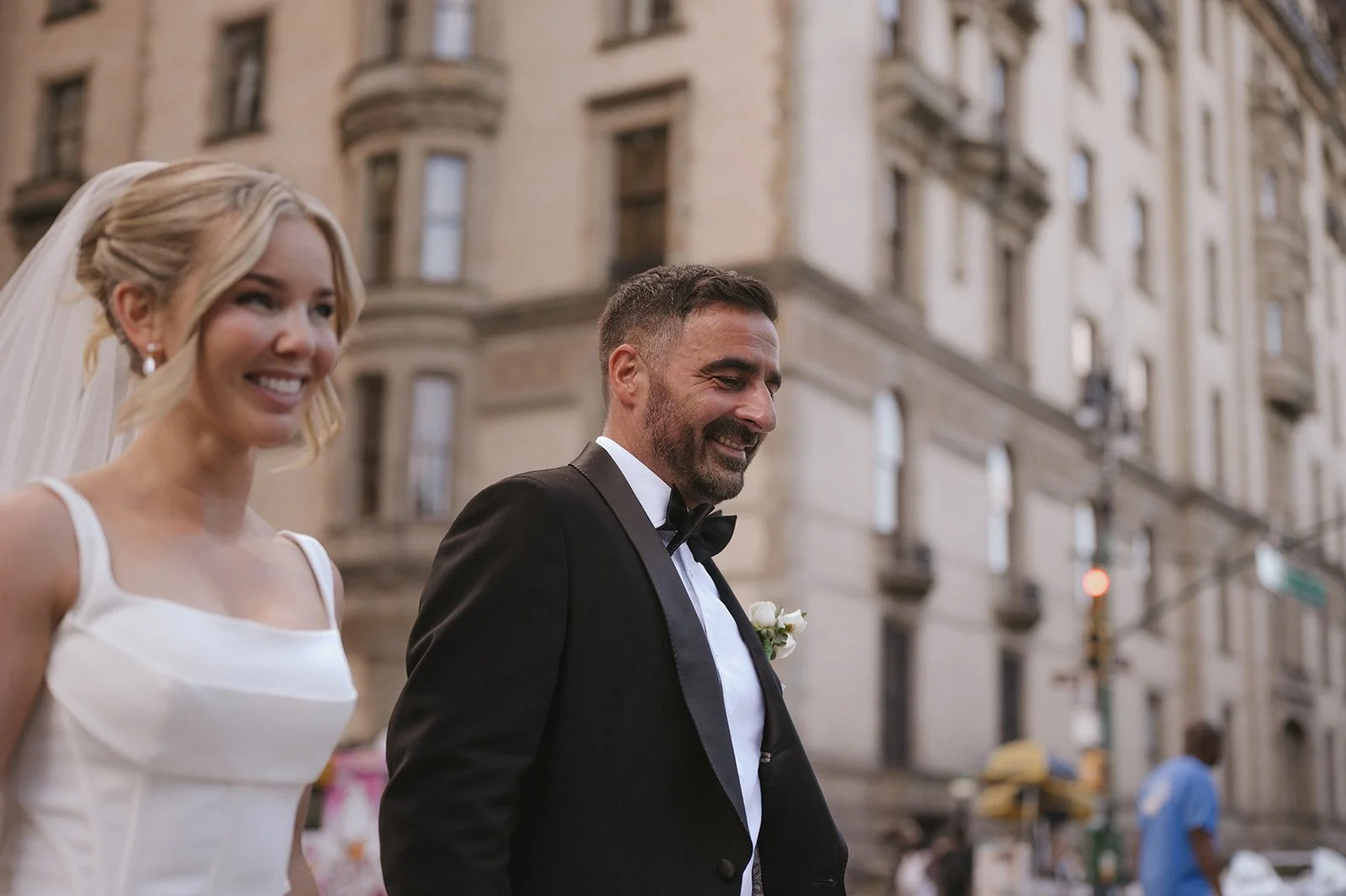 Bride and groom walking and smiling with the buildings of Manhattan behind them.