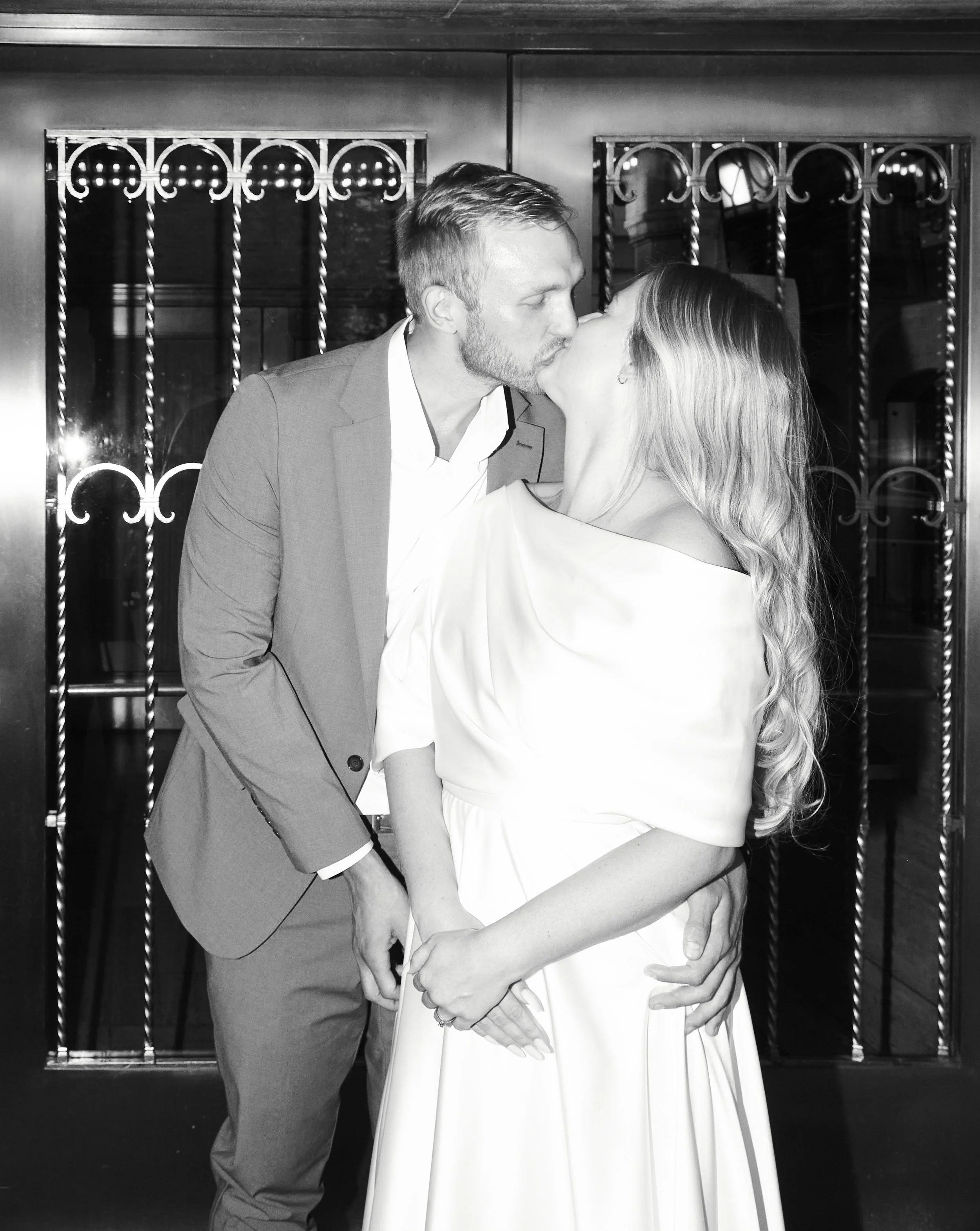 Bride and groom kissing in front of the doors at the Al Hirschfeld Theatre where Moulin Rouge! is playing.