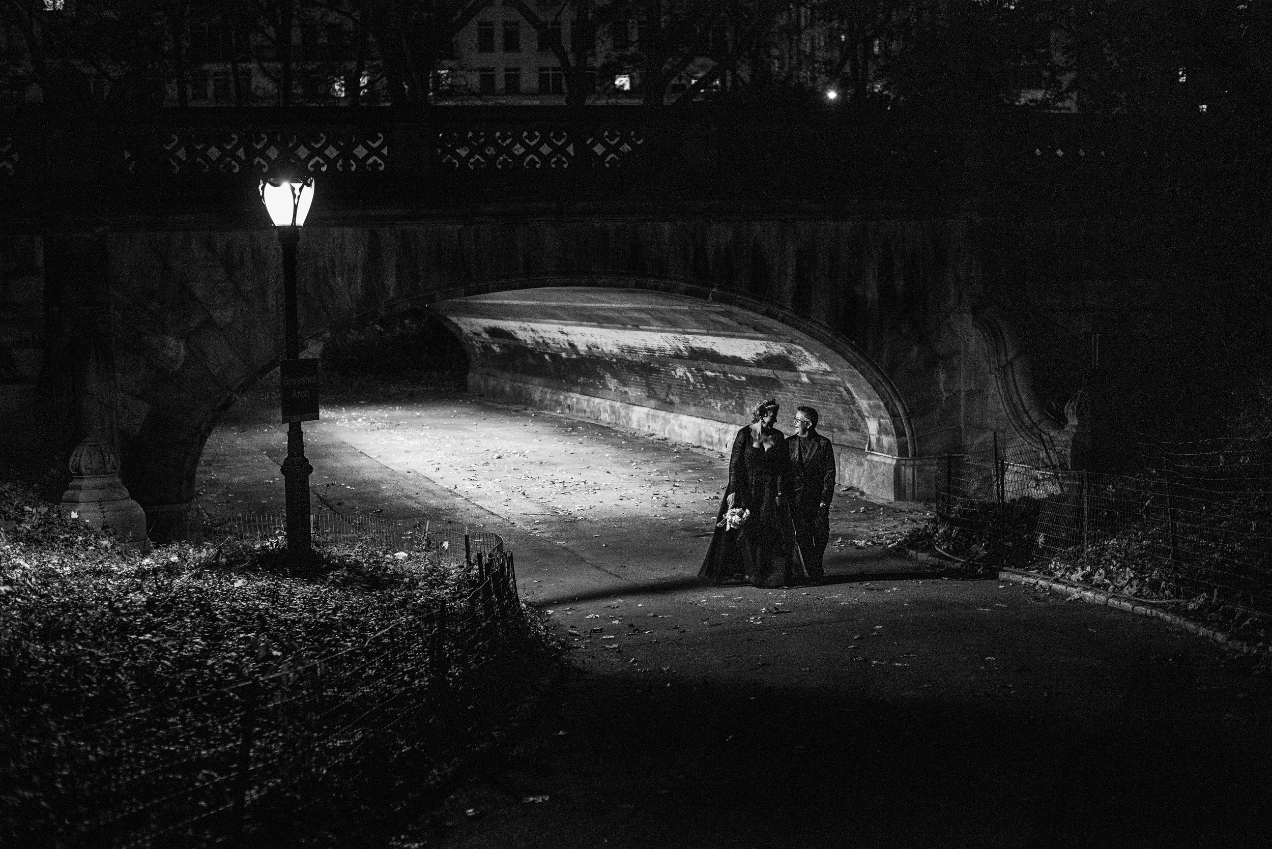 Two brides walking under a bridge in Central Park at night after their LGBTQ-friendly Cakewalk elopement.