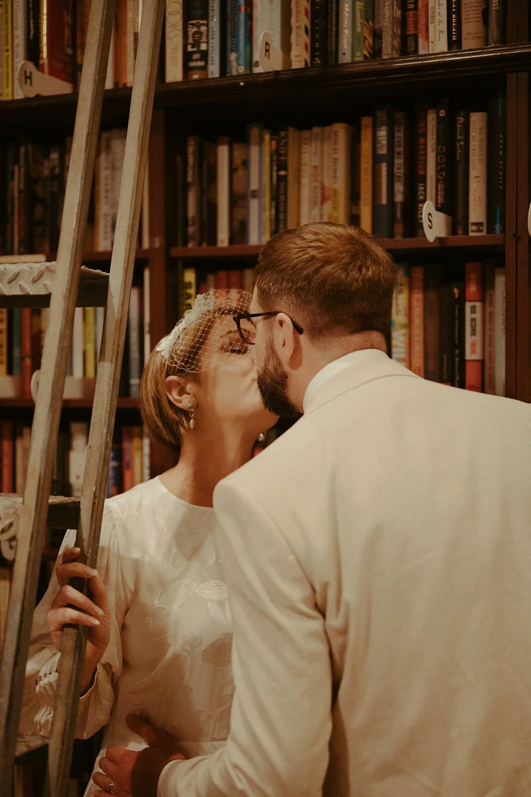 Bride and groom kissing next to a ladder by the bookcases at Housing Works Bookstore in SoHo after their Cakewalk elopement.