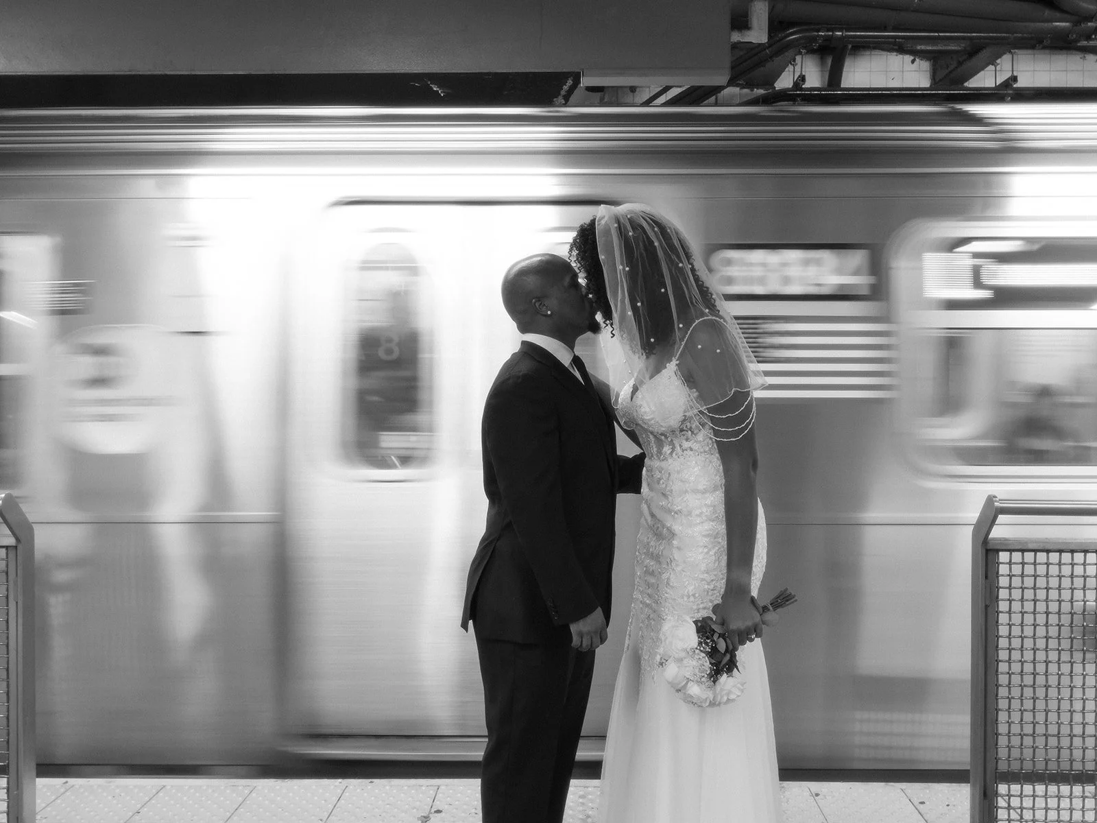 Bride and groom kissing in front of a moving train in a subway station in New York City after their Cakewalk elopement.