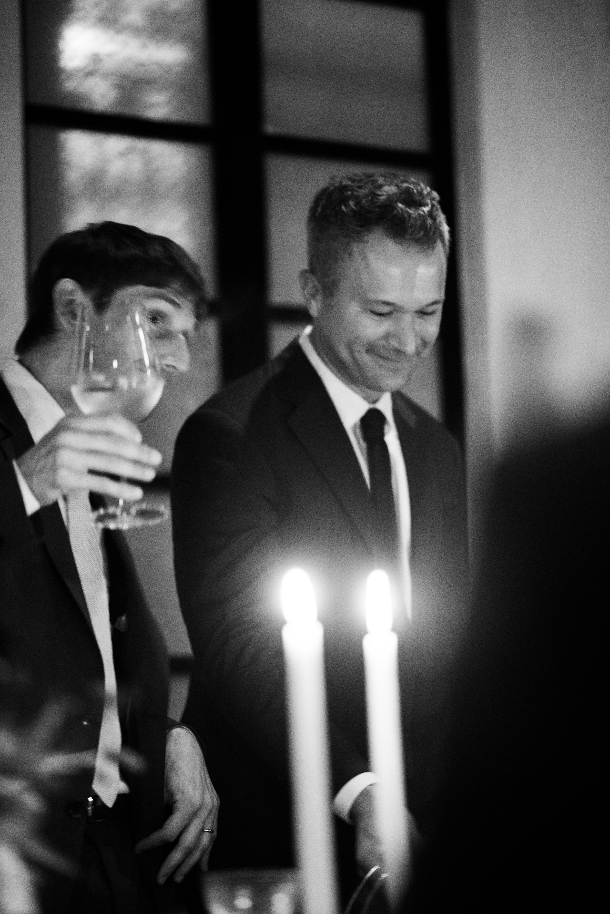 Two men at wedding reception holding drinks and standing around the table candles.