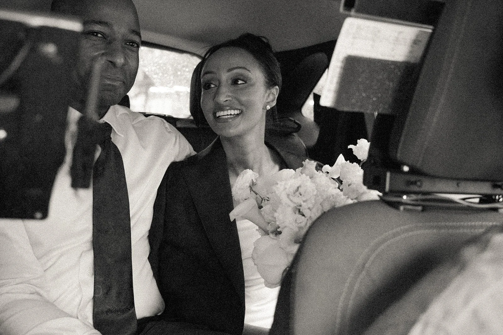 Bride and groom smiling, seated in the back of a New York taxi after their Cakewalk wedding ceremony.