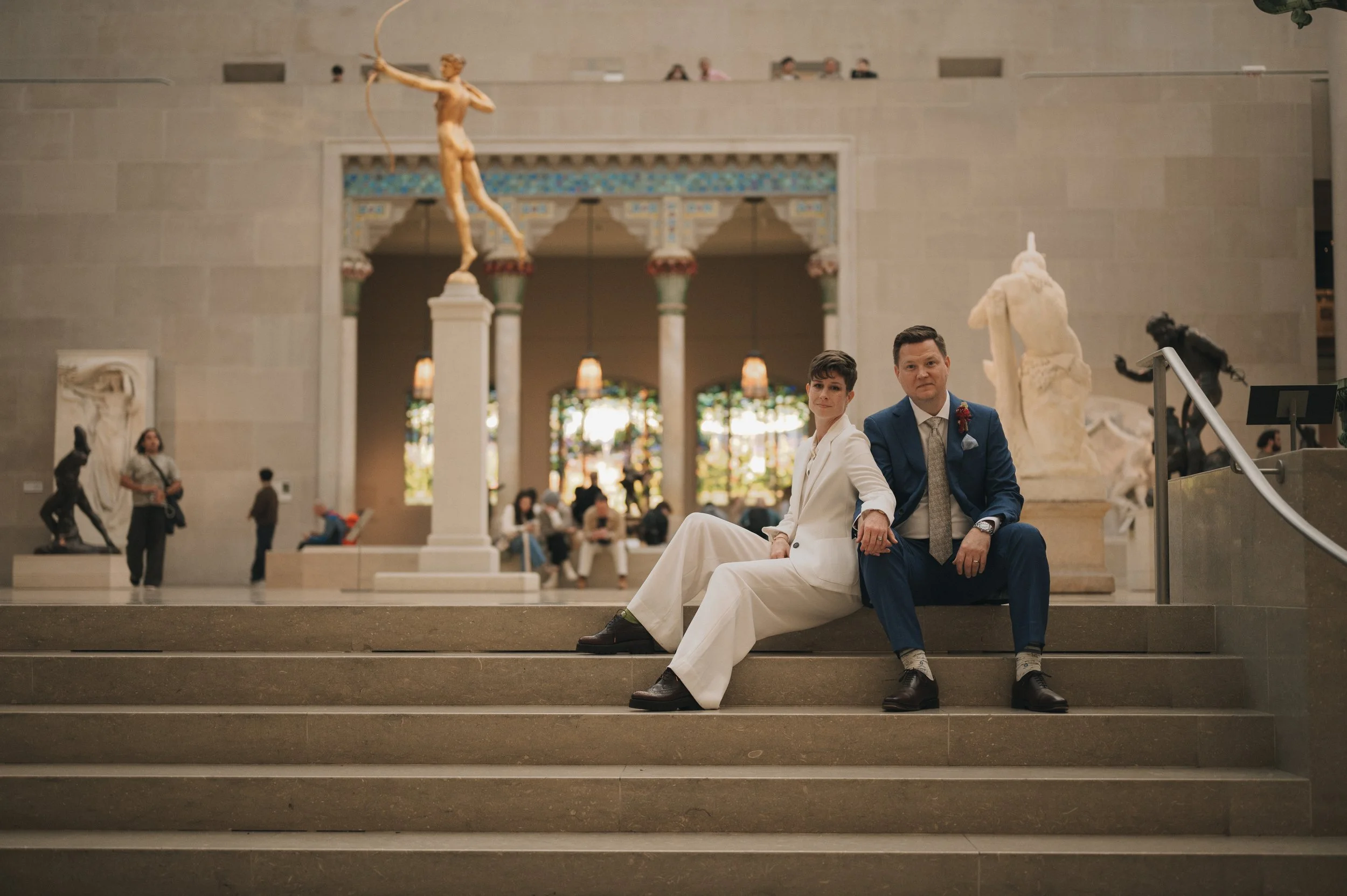 Couple seated on the steps of The Met’s sculpture court surrounded by statues and soft light.