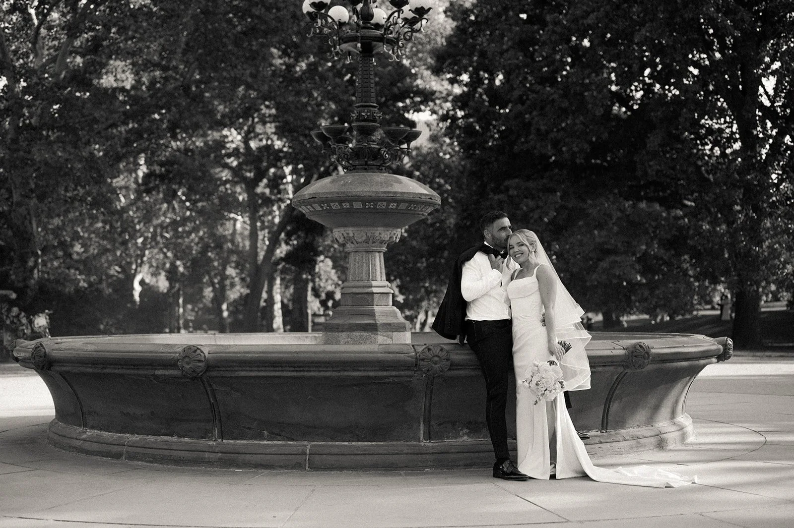Bride and groom posing in front of a fountain in Central Park.