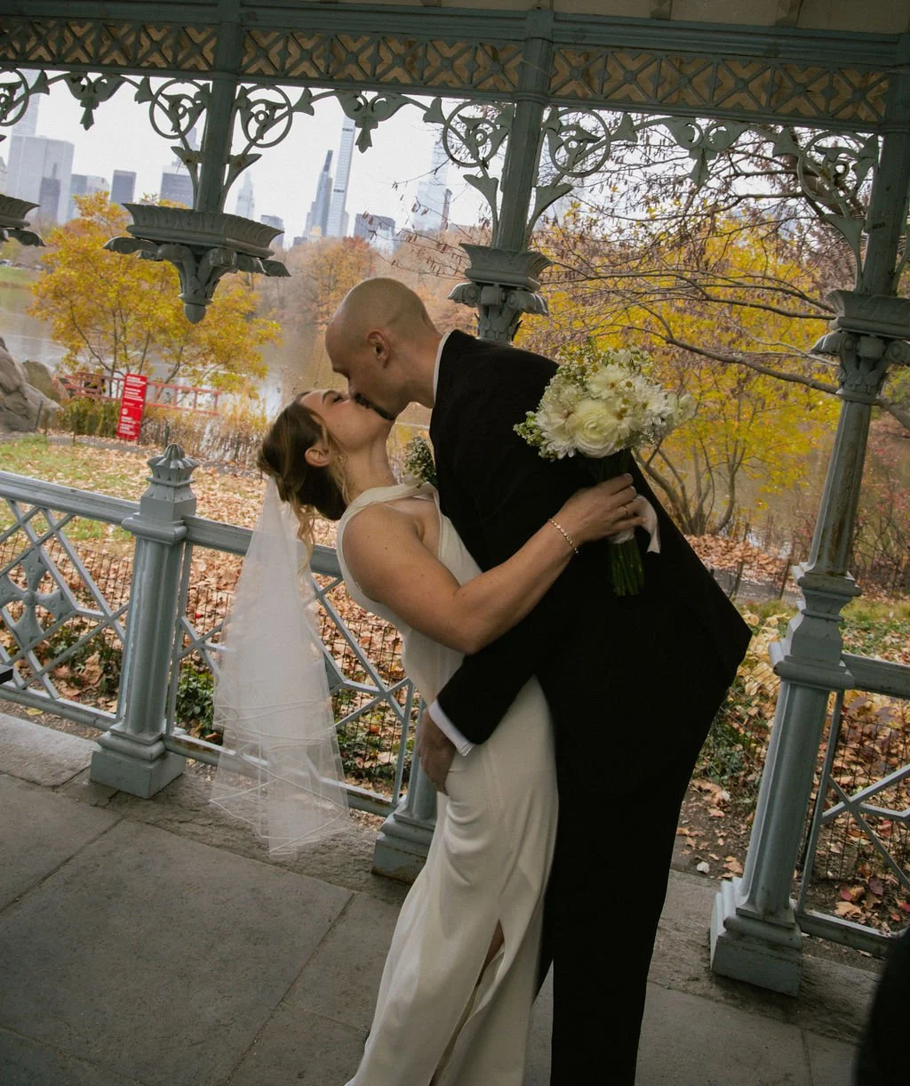 Couple kissing under Ladies Pavilion gazebo in Central Park during their NYC elopement with autumn foliage and skyline views