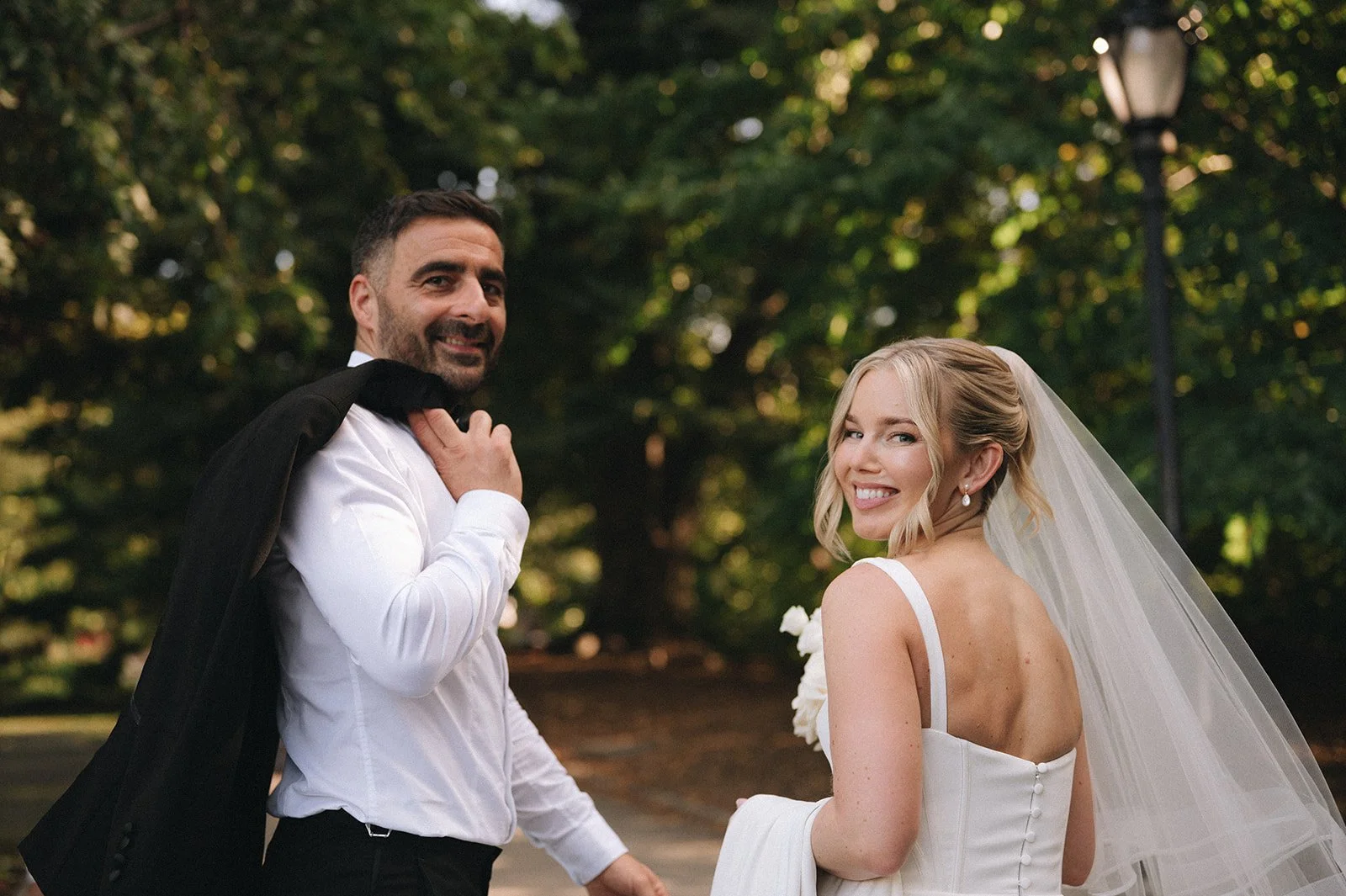 Bride and groom looking over their shoulders smiling after their Cakewalk wedding ceremony in Central Park.