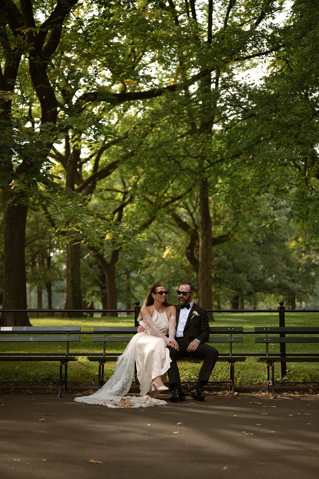 Bride and groom seated on Central Park bench, surrounded by lush trees after their Cakewalk elopement ceremony.