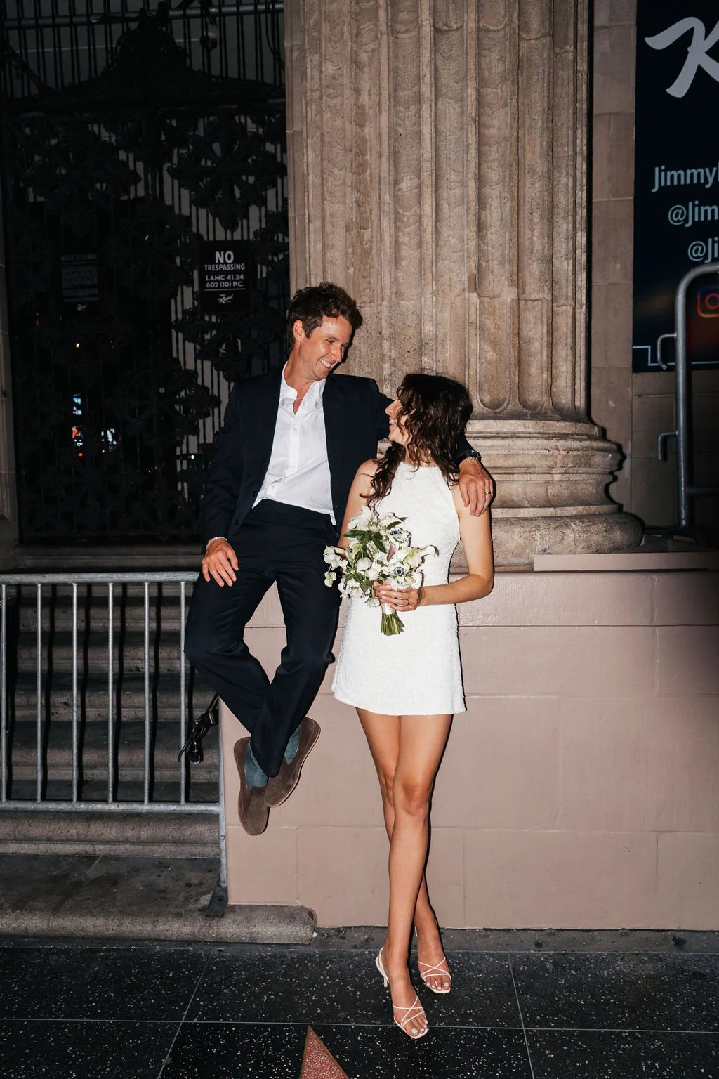 Couple posing in front of a column on Hollywood Blvd at night in wedding attire.