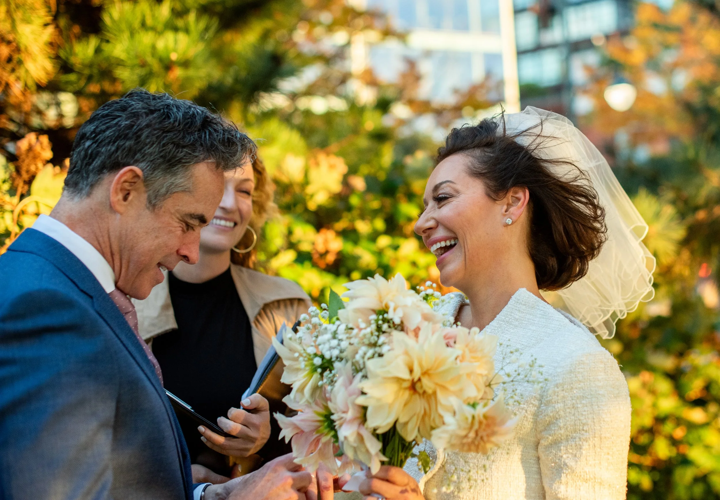 Bride and groom being married at Hudson River Park, bouquet in hands, with officiant smiling behind them.