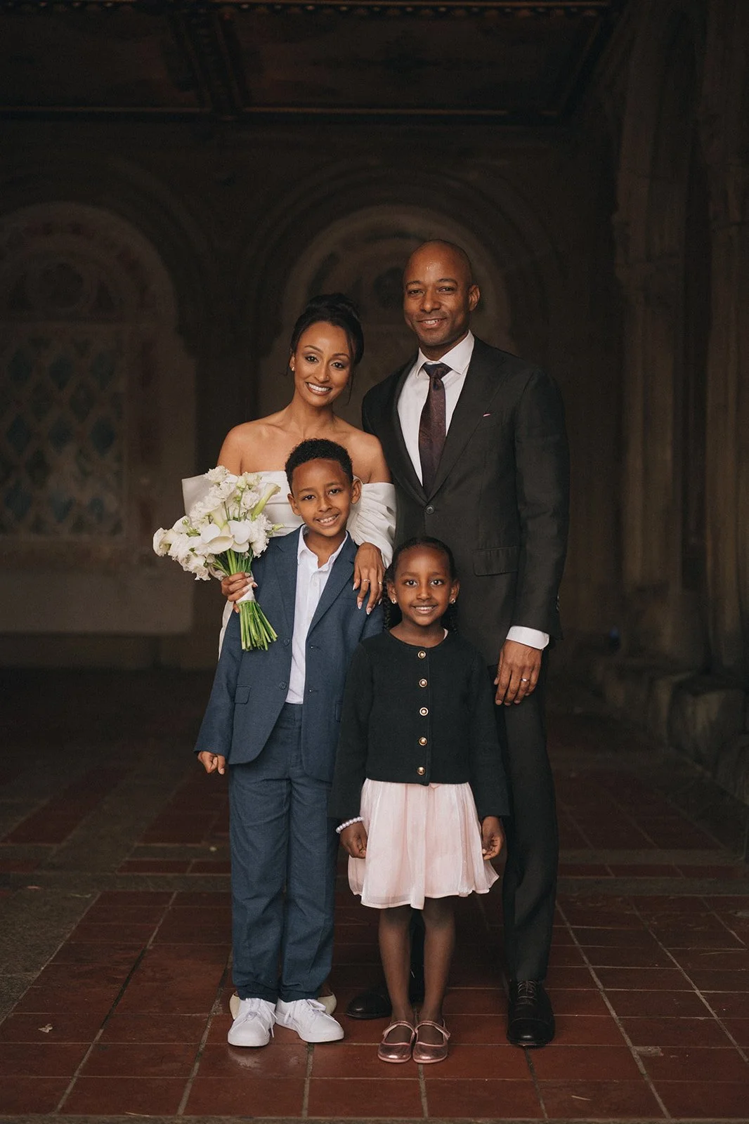 Bride and groom posing for a family portrait with children at Bethesda Terrace after their micro wedding ceremony.