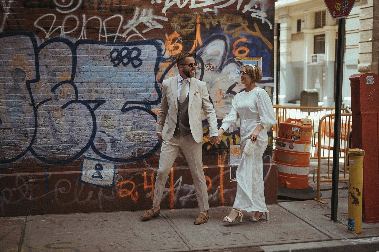 Couple walking hand in hand past a graffiti-covered wall during post-ceremony elopement photos in NYC.