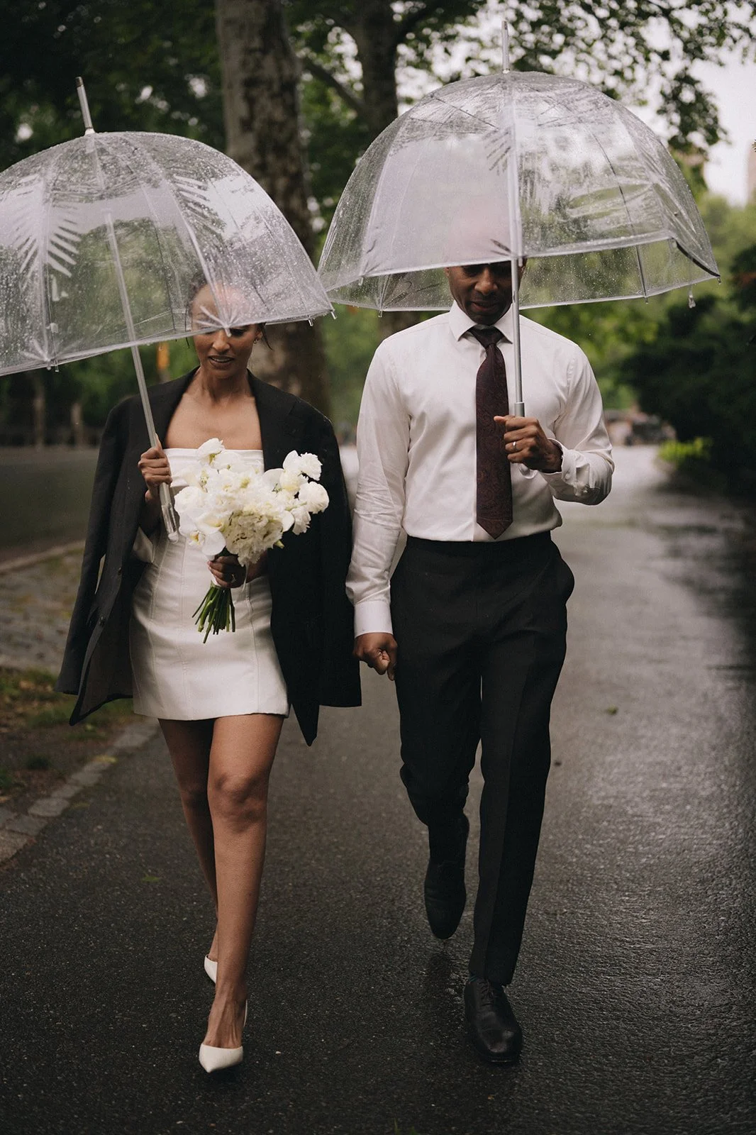 Bride and groom holding clear umbrellas, walking in the street after their Cakewalk wedding ceremony.