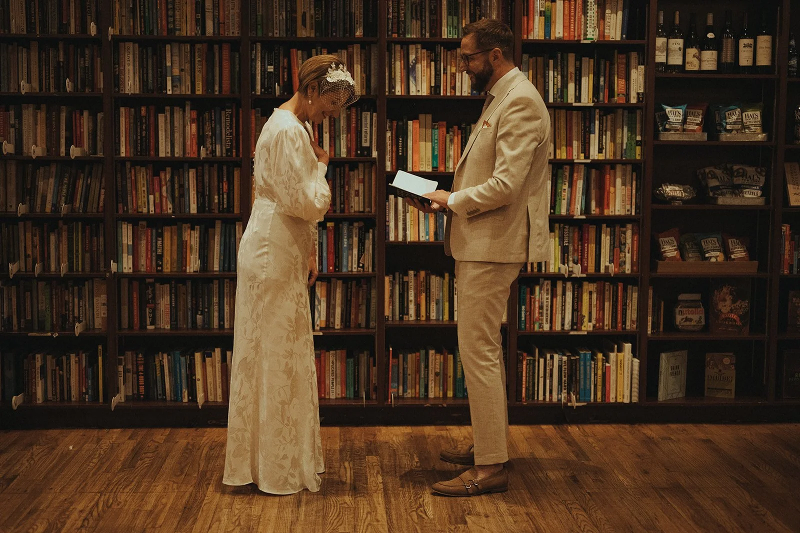 Bride and groom reading each other vows in front of tall bookcases inside Housing Works Bookstore in SoHo during Cakewalk elopement ceremony.
