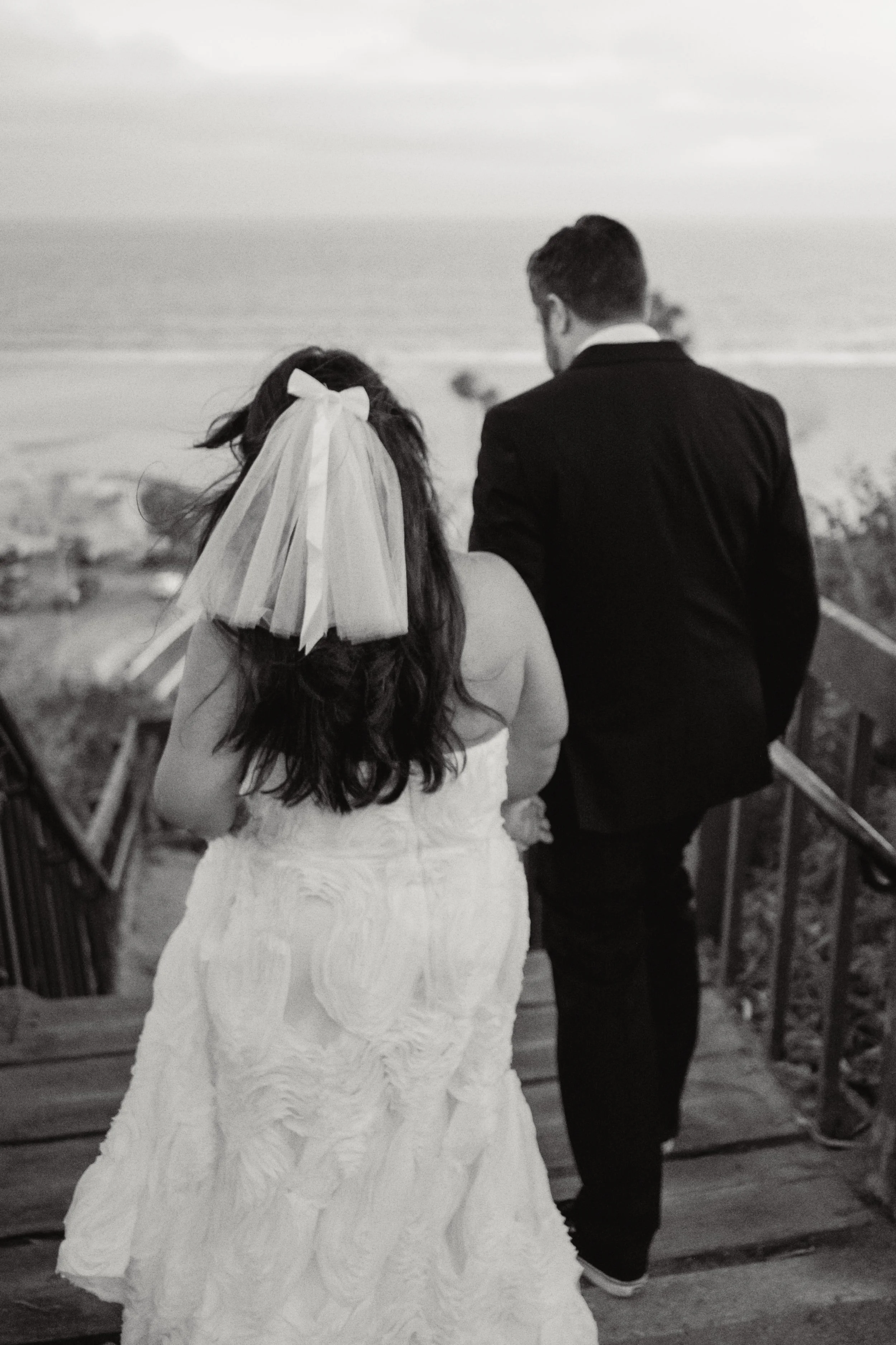 Bride and groom walking down the cliffside steps in Santa Monica with the the sand and the ocean behind them.