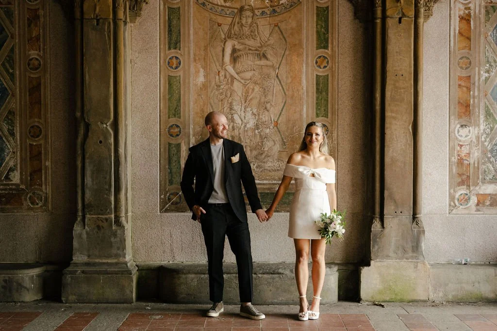 Bride and groom posing in front of wall art at Bethesda Terrace in Central Park, on the way to their Cakewalk elopement.