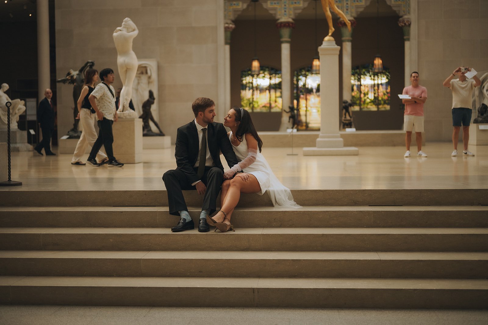 Bride and groom sitting on the step inside the Met Museum of Art among the sculptures.