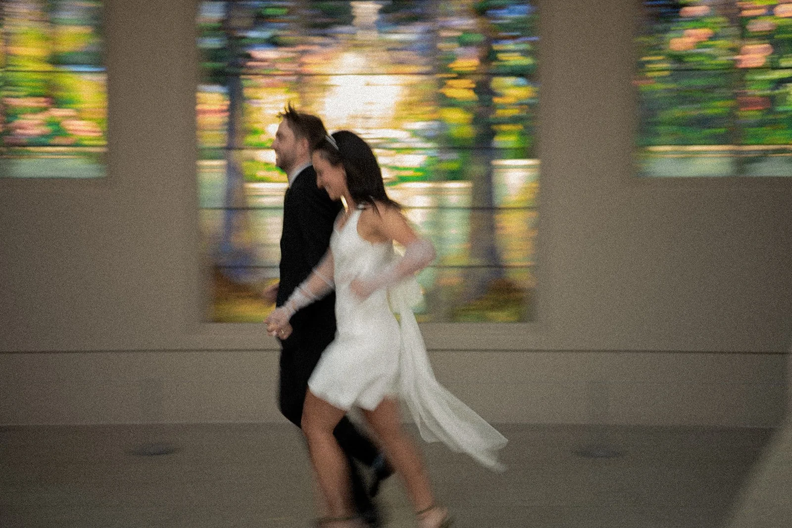 Bride and groom running inside the Met Museum of Art with stained glass windows behind them.