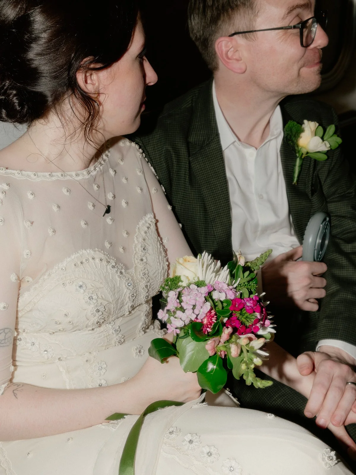 Bride and groom seating on the subway in New York City, holding hands.