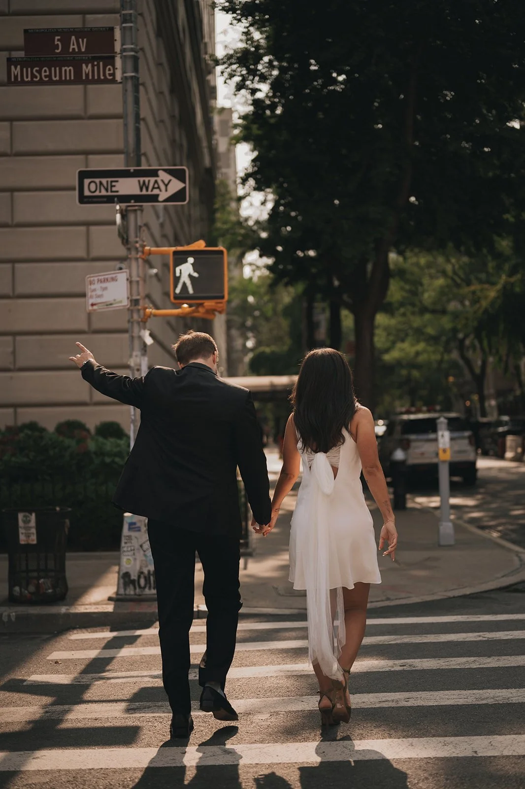 Kayla and Zach holding hands while crossing Fifth Avenue near the Metropolitan Museum of Art on their NYC elopement day.