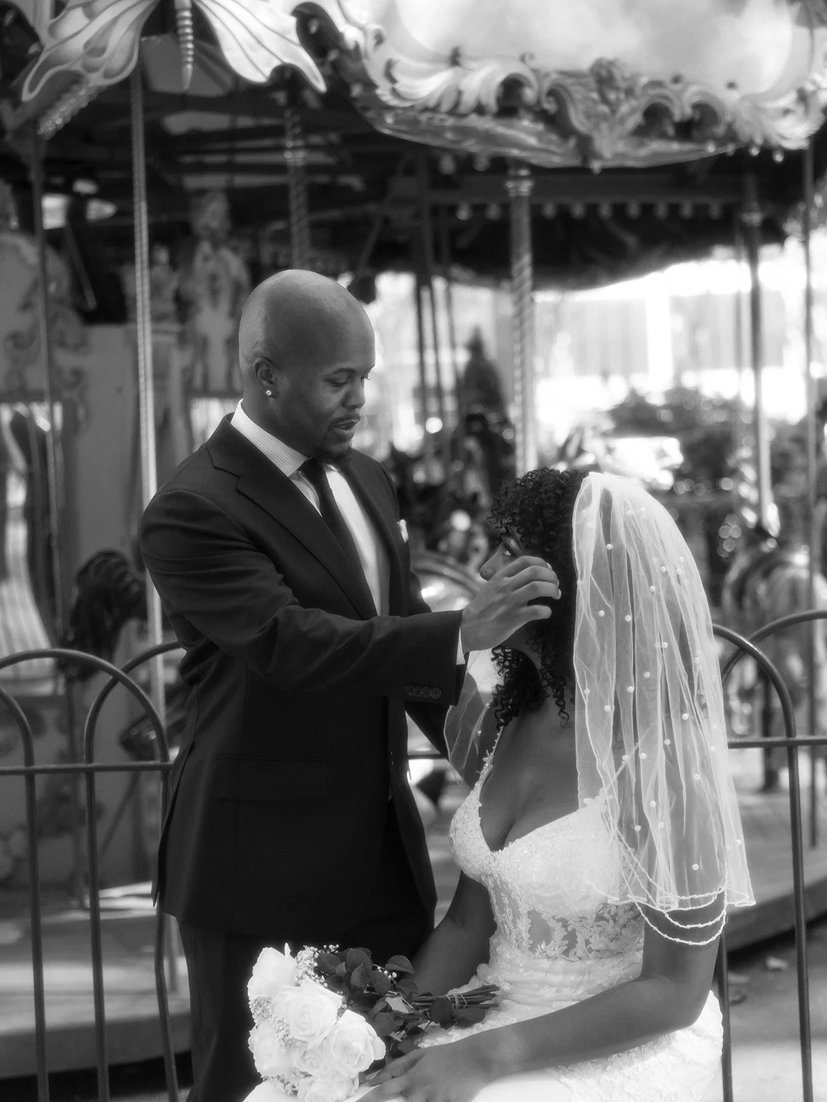 Bride and groom seated in front of an ornate carousel, looking at each other in Bryant Park after their wedding ceremony.