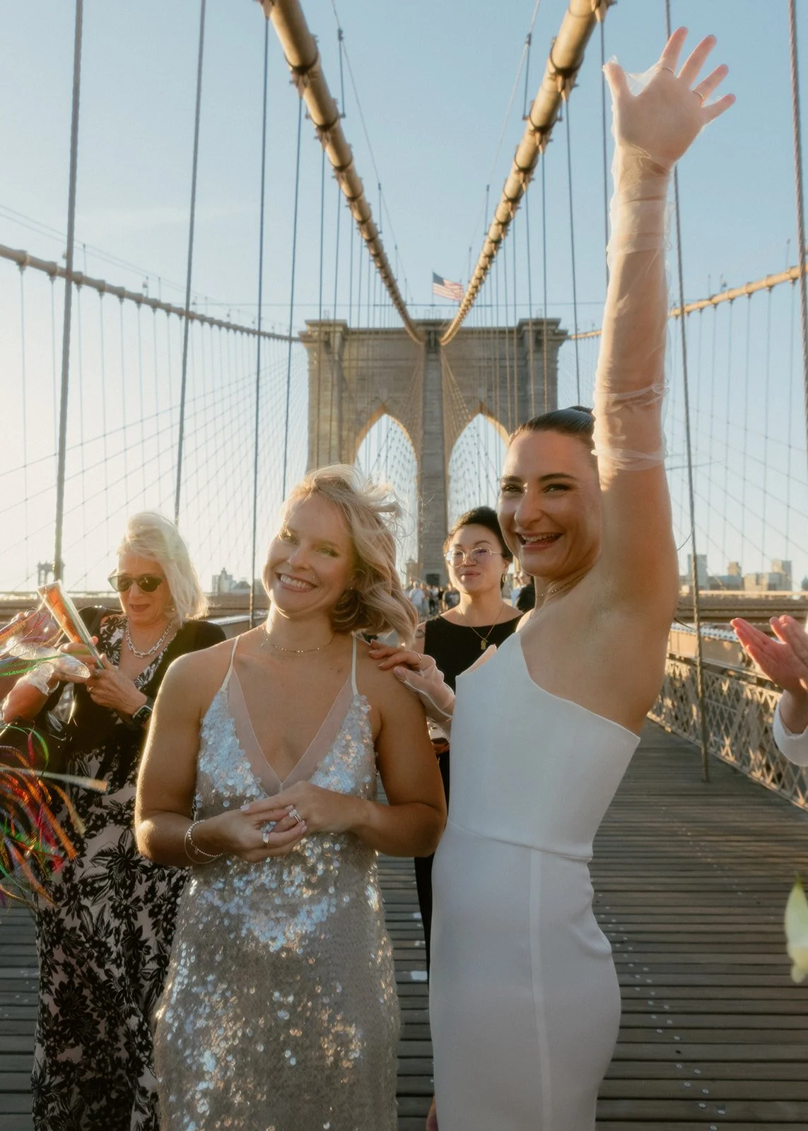 Newly married couple celebrate after their Brooklyn Bridge elopement at sunrise, surrounded by friends and golden morning light.