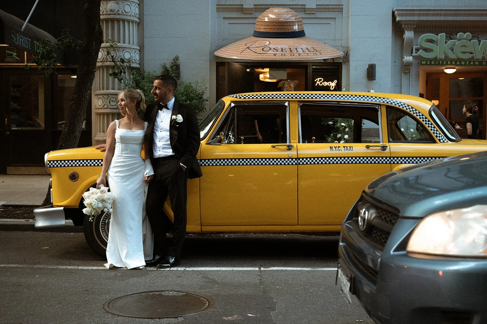 Bride and groom posing in front of a vintage, yellow checkered NYC taxi in front of Rosehill.