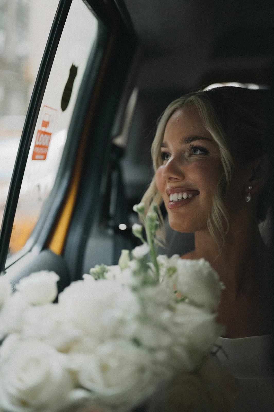 Bride riding to her Cakewalk elopement in a taxi, smiling and holding a white bouquet.