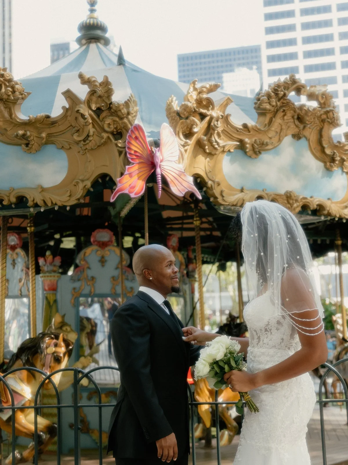 Bride and groom standing in front of an ornate carousel, looking at each other in Bryant Park.