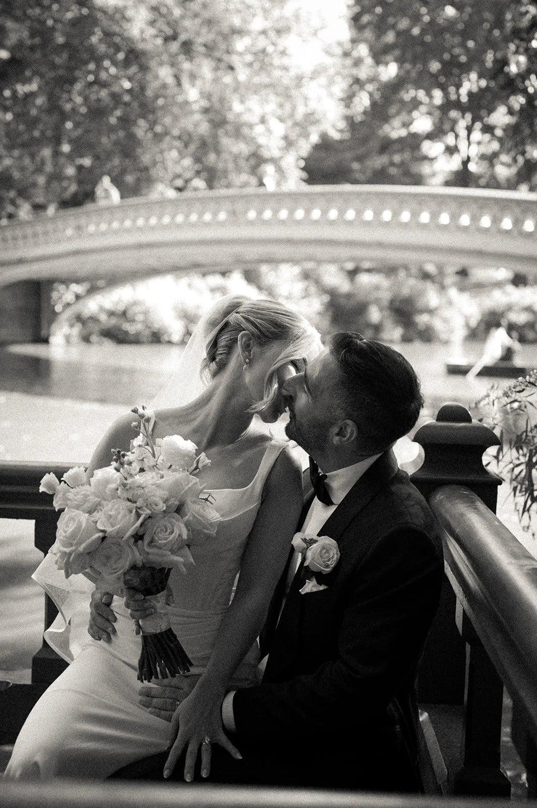 Bride and groom kissing in front the water and Bow Bridge in Central Park.