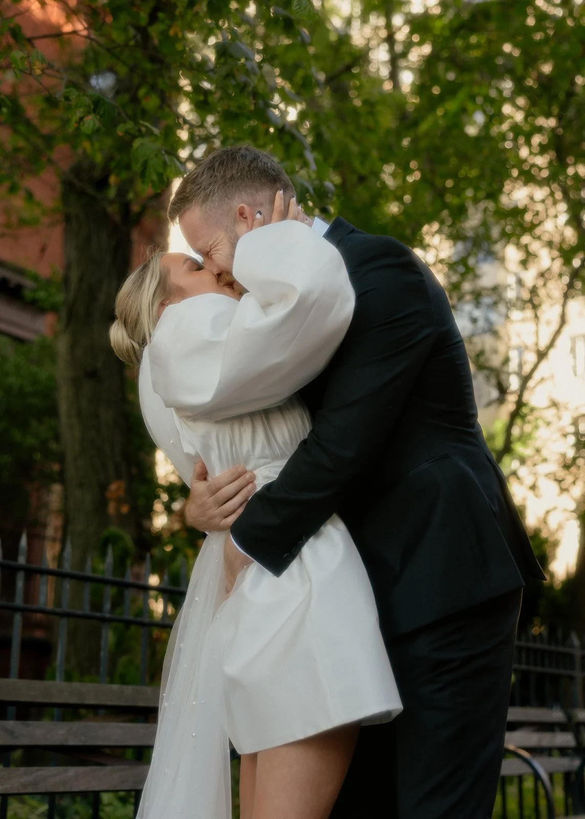 Bride and groom kissing with trees and brownstones behind them during Brooklyn elopement ceremony by Cakewalk.