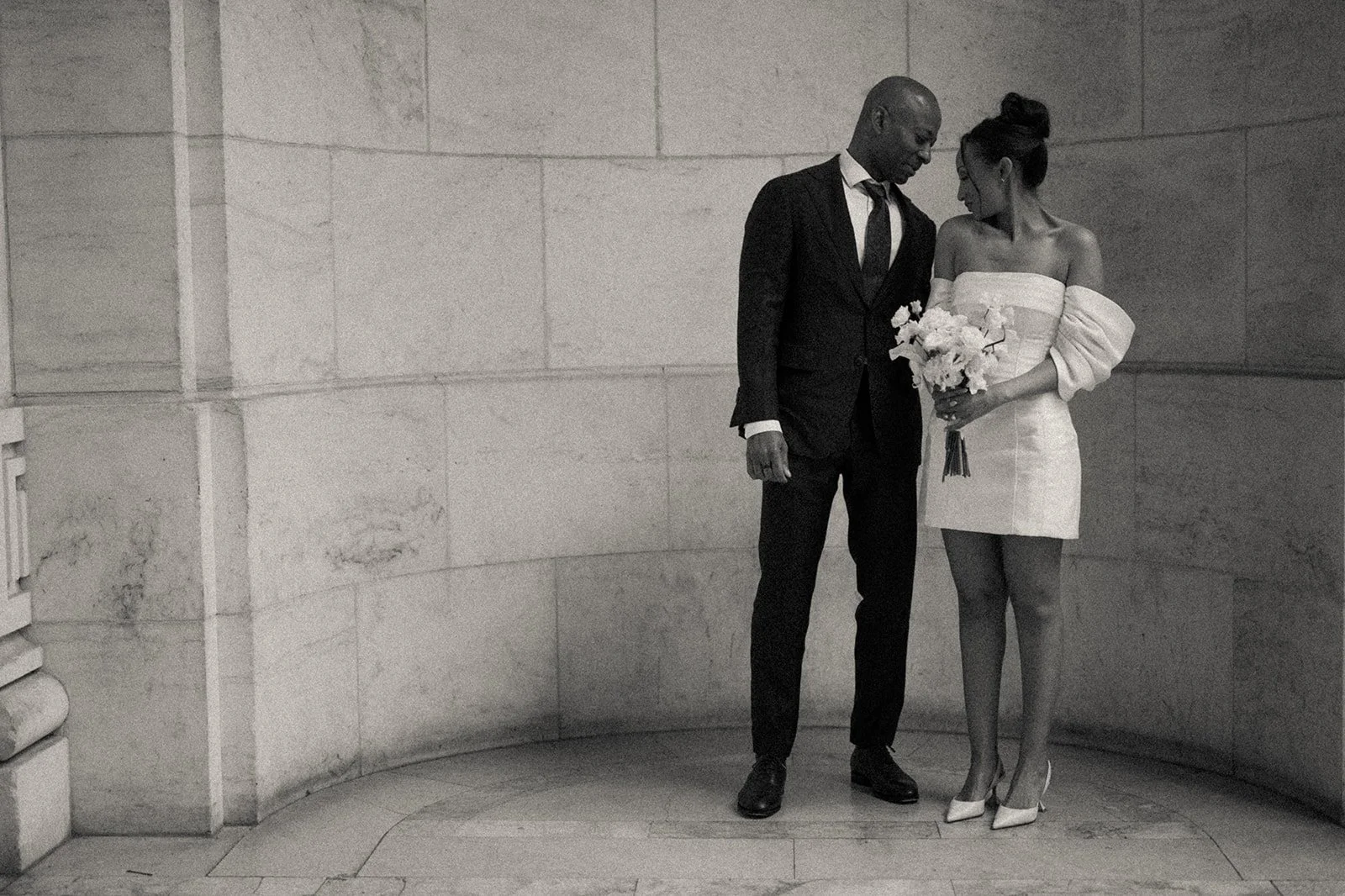 Bride and groom posing by a rounded wall at the New York Public Library after their Cakewalk wedding ceremony.