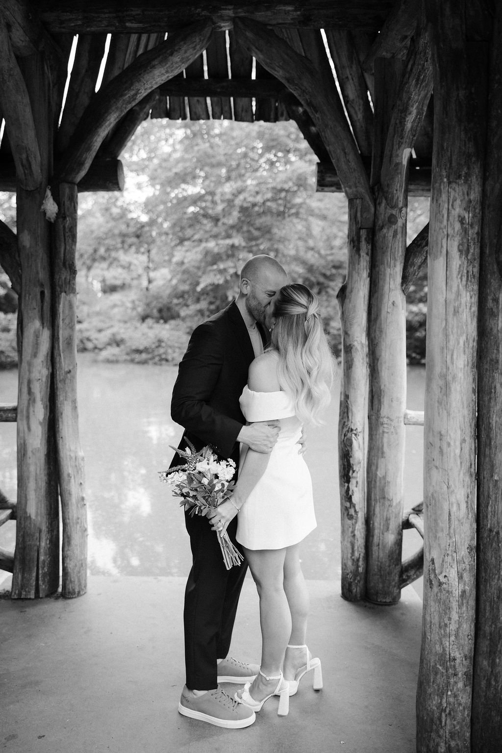 Black and white photo of Chloe and Sam on a Central Park bridge with the cityscape behind them after their Wagner Cove elopement.